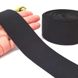 May include: Black grosgrain ribbon, a type of fabric ribbon with a textured, woven surface, shown rolled up and laid flat.