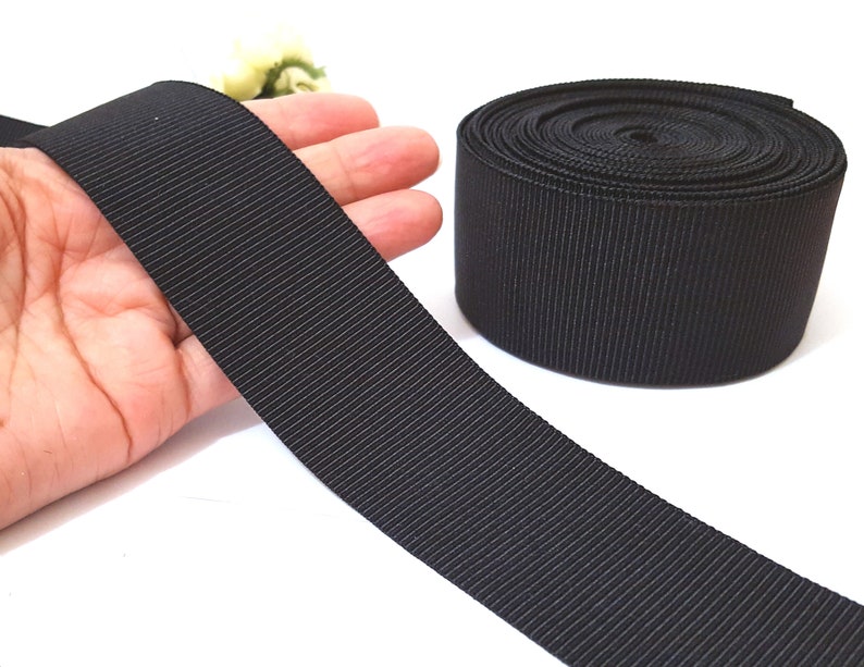 May include: Black grosgrain ribbon, a type of fabric ribbon with a textured, woven surface, shown rolled up and laid flat.