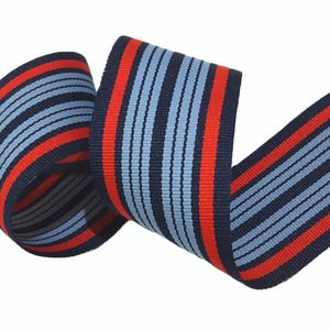 May include: Red and blue striped ribbon with a woven texture. The ribbon is folded and twisted, showing the pattern.