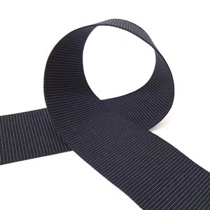 May include: A black grosgrain ribbon with a ribbed texture. The ribbon is folded in a loop shape.
