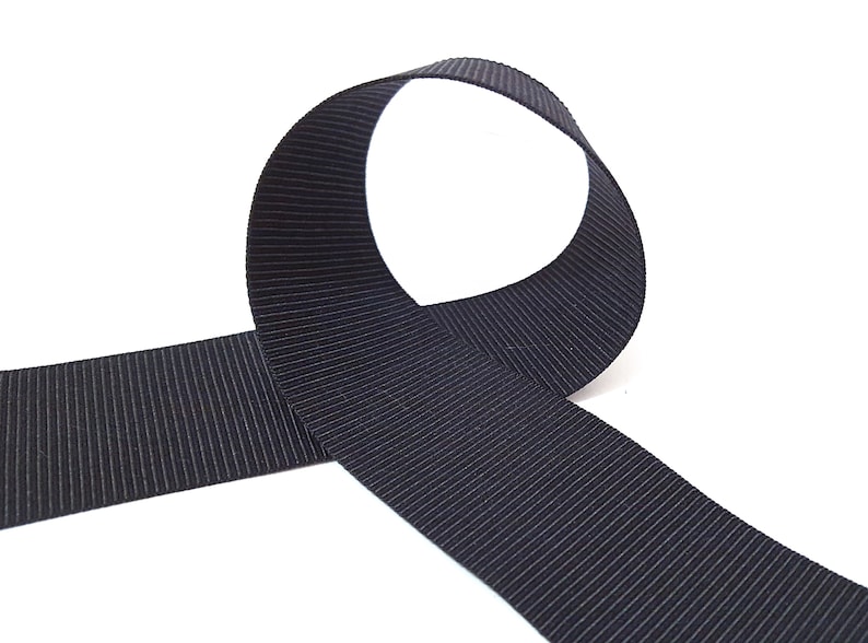 May include: A black grosgrain ribbon with a ribbed texture. The ribbon is folded in a loop shape.