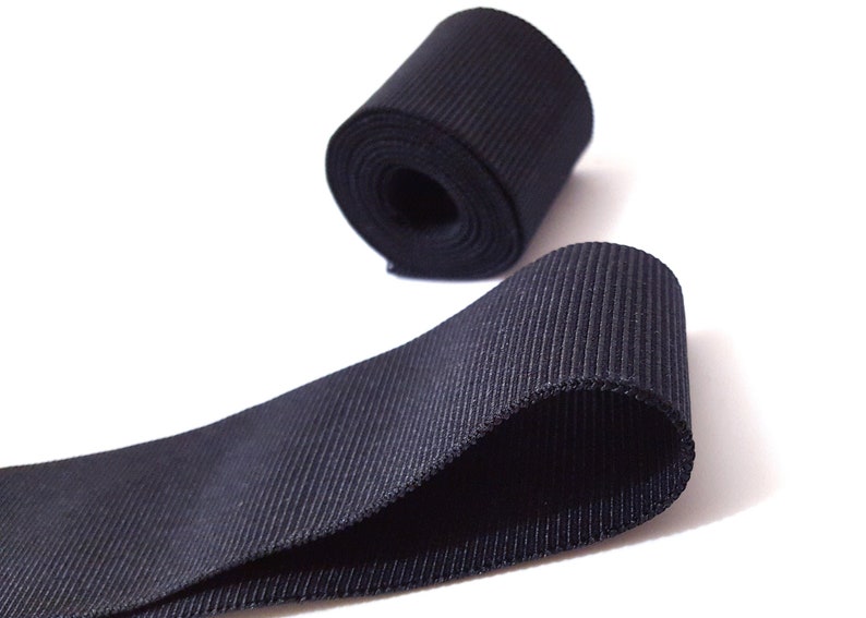 May include: A roll of black grosgrain ribbon. The ribbon is folded in half and the ends are overlapping. The ribbon is about 1 inch wide.