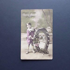 Antique Happy New Year Postcard. Little boy bringing good luck. Horseshoe. Holly branches. Holiday season. French postcard