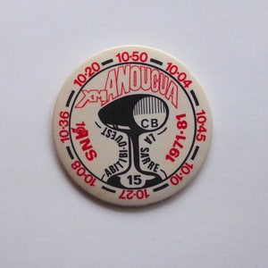 May include: A white circular token with black and red text. The text reads "10-36 10-08 10-20 - 10-50 - 10-04 10-45 10-10 1971-81 - 10-01-10-27 15 ANS QUEST AB SARRE CB LA ANOUCVA".
