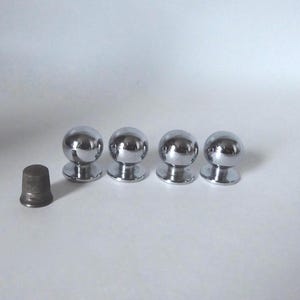 以下が含まれることがあります： 球状のデザインの光沢のあるクロム仕上げのキャビネットノブが4つ、小さな濃い色の指ぬきの隣に表示されています。ノブは円形のベースと反射面を持ち、モダンな美しさを暗示しています。