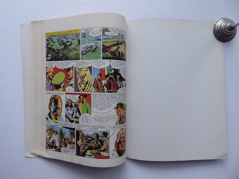 May include: A comic book open to a page with colourful illustrations of people and a landscape. The page is filled with speech bubbles and text. The right page is blank.
