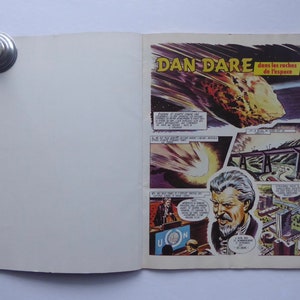 May include: A comic book cover featuring a man with a white beard and the title "Dan Dare dans les roches de l'espace". The cover depicts a large asteroid hurtling towards Earth.