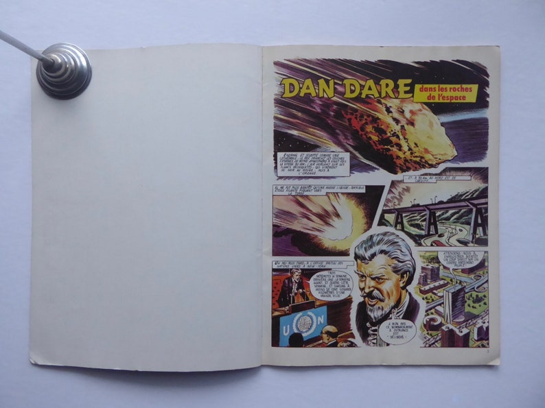 May include: A comic book cover featuring a man with a white beard and the title "Dan Dare dans les roches de l'espace". The cover depicts a large asteroid hurtling towards Earth.