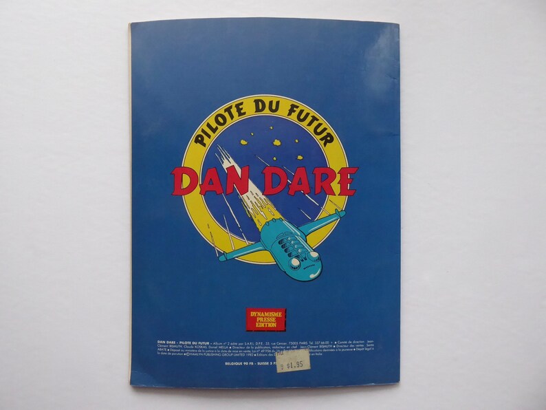 May include: A blue and yellow comic book cover with the title "PILOTE DU FUTUR DAN DARE" in red and white letters. The cover features a blue and white spaceship flying through a yellow and white trail.