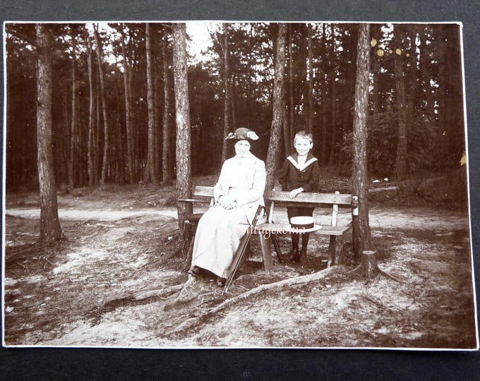 Photo of woman and child. Black and white glossy paper 1910. Woman sitting on bench. Forest. Sailor suit. Sailor hat. Flower hat. Cane