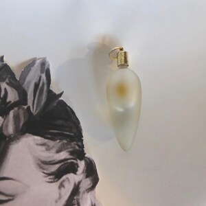 May include: A clear glass perfume bottle with a gold top and a pearlescent finish. The bottle is shaped like a teardrop and has a small, round opening at the top.