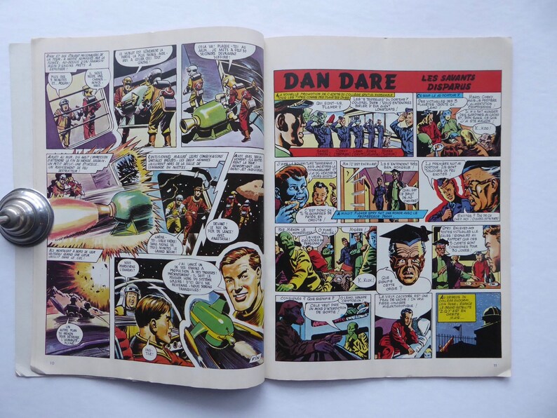 May include: A comic book page from the series "Dan Dare" featuring a colourful illustration of a rocket ship and a group of people in a futuristic setting. The text on the page reads "Dan Dare" and "Les Savants Disparus".