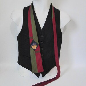 May include: A black vest with a patterned tie. The tie features red, green, and blue stripes, with a small emblem. The tie is draped over a white mannequin. The bottom of the tie has text.