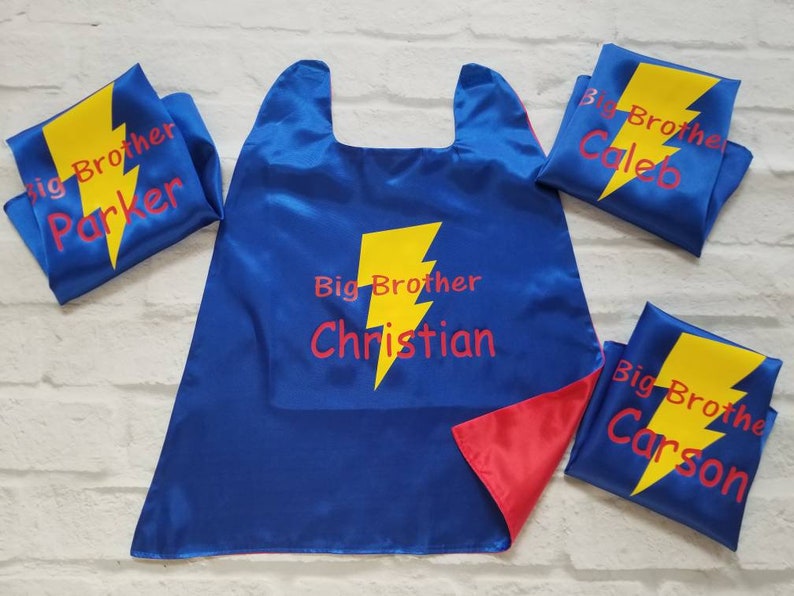 May include: Blue satin superhero capes and matching masks with yellow lightning bolt designs. The capes and masks have the words "Big Brother" and individual names in red. The cape is reversible with a red interior.
