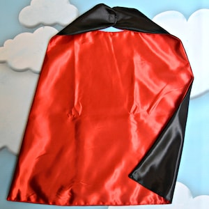 May include: A reversible cape, red on one side and black on the other. The cape is made of a shiny, satin-like material. The cape is designed to be worn around the neck.