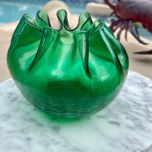 May include: A green glass bowl with a ruffled edge and a textured surface. The bowl is made of clear glass and has a light green tint.