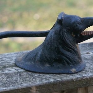 May include: A black cast iron nutcracker shaped like a bear's head with an open mouth and sharp teeth. The bear's head is on a base with a long handle.
