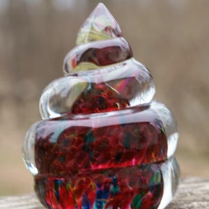 May include: A glass paperweight with a spiral design. The paperweight is made of clear glass with red, blue, and green swirls.