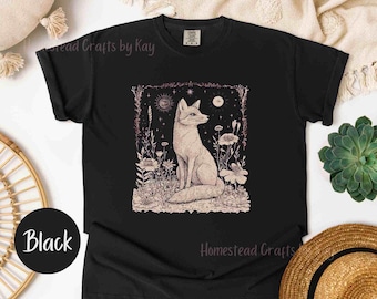 May include: Black t-shirt with a graphic of a fox sitting in a field of flowers and stars. The fox is white with a pink nose and tail. The text "Homestead Crafts" is at the bottom of the shirt.