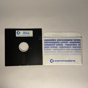 May include: A black floppy disk with a white label that reads "Zork II C64626 Commodore Business Machines, Inc."  The disk is in a white paper sleeve with the text "commodore microcomputer-system microcomputer-system * commodor ocomputer-system * commodore mi puter-system * commodore microco system * commodore microcompute commodore microcomputer-system microcomputer-system * commodor commodore" printed in blue.