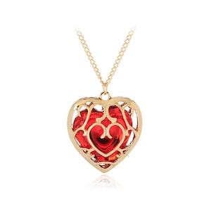 May include: Gold necklace with a red heart-shaped pendant. The pendant is a cage-like design with a red heart inside.