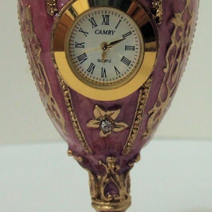 Russian Replica Purple Enameled Faberge egg with a golden clock displayed with gold decor and gem bands.