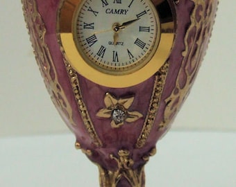 Russian Replica Purple Enameled Faberge egg with a golden clock displayed with gold decor and gem bands.