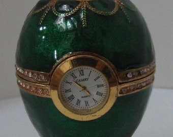 Russian Replica Green Enameled Faberge egg with a golden clock displayed and elephant on top with gold decor and gem bands.