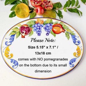 May include: Oval ceramic tile with a painted design of grapes, pomegranates, and leaves. The tile is white with blue and yellow accents. The text "Please Note: Size 5.15" x 7.1" / 13x18 cm comes with NO pomegranades on the bottom due to its small dimension" is printed on the tile.