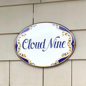 Oval Ceramic House sign hand-painted  with a blue and yellow design on the sides. The name is painted in blue cursive