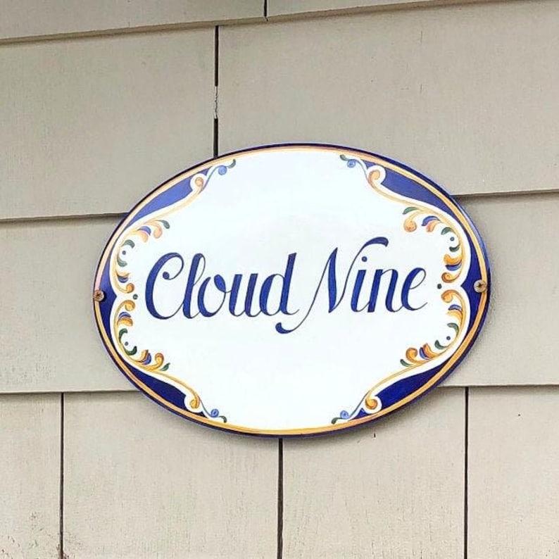 Oval Ceramic House sign hand-painted  with a blue and yellow design on the sides. The name is painted in blue cursive