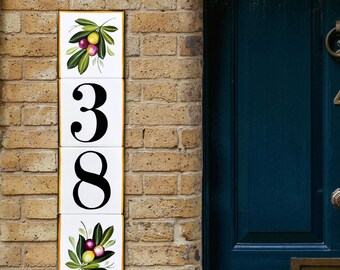 May include: White ceramic tiles with black numbers 38 and a floral design with green leaves and purple and yellow berries. The tiles are mounted on a brick wall next to a dark blue door.