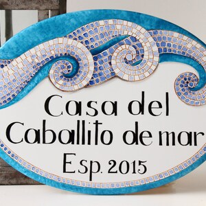 May include: Oval ceramic sign with a blue and white mosaic design depicting waves. The sign reads "Casa del Caballito de mar Esp. 2015".