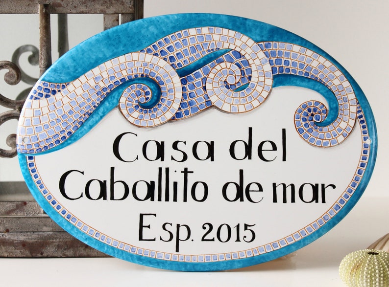 May include: Oval ceramic sign with a blue and white mosaic design depicting waves. The sign reads "Casa del Caballito de mar Esp. 2015".