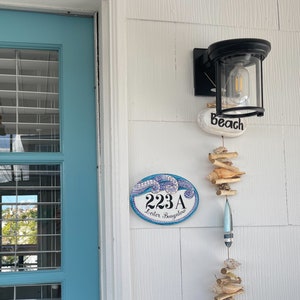 a blue and white tile sign hand painted with waves in mosaic stylet: house number and address painted in black are shown in the center of the plaque