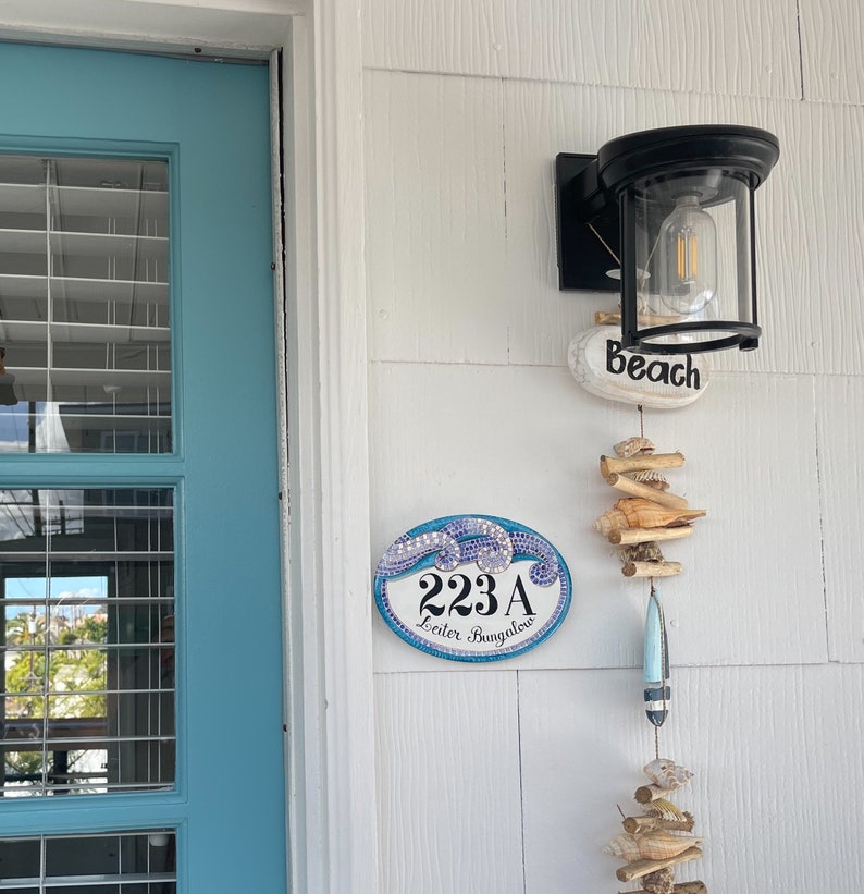 a blue and white tile sign hand painted with waves in mosaic stylet: house number and address painted in black are shown in the center of the plaque