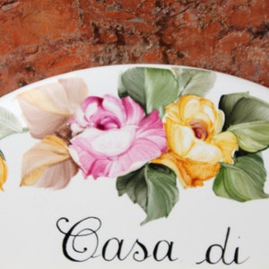 May include: White ceramic oval plate with a painted floral design of pink and yellow roses with green leaves. The plate has the text "Casa di" written in black cursive.