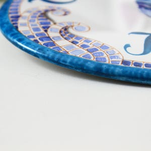May include: A blue and white ceramic plate with a mosaic design and the word "Home" written in blue.