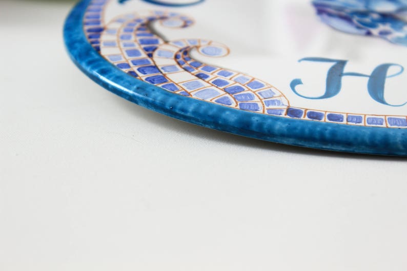 May include: A blue and white ceramic plate with a mosaic design and the word "Home" written in blue.