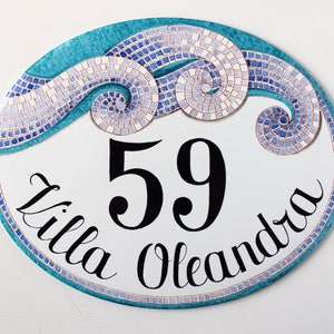 A white oval ceramic sign with a blue and white mosaic design. The sign has the number 59 and the text "Villa Oleandra" written in black cursive.