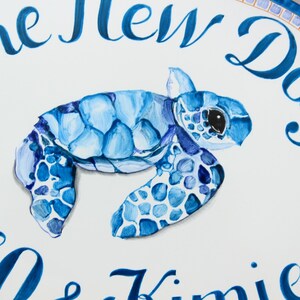 May include: A white oval sign with blue and gold mosaic trim. The sign says "The New Day" in blue cursive lettering. A blue painted sea turtle is in the center of the sign. Below the turtle, the sign says "Ho & Kimie" in blue cursive lettering.