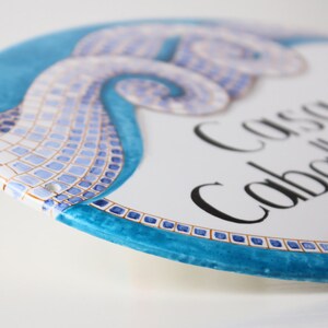 A white ceramic oval sign with a blue mosaic design. The sign reads "Casa del Caballito de Mar".