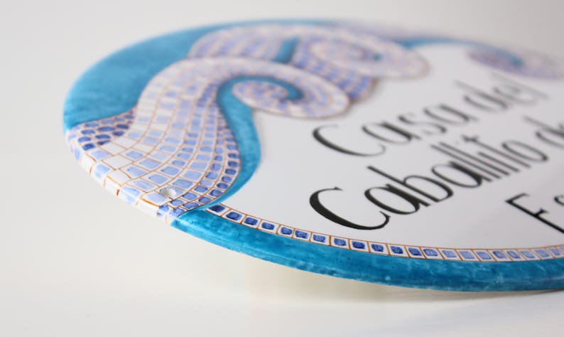 A white ceramic oval sign with a blue mosaic design. The sign reads "Casa del Caballito de Mar".