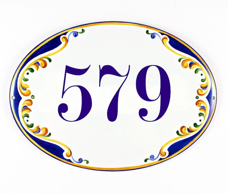 Oval ceramic house number sign with the number 579 painted in a deep purple font. The sign is hand-painted with a blue and gold decorative border. The border features ornate floral designs.