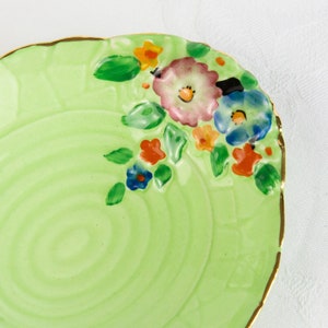 May include: A green ceramic saucer with a gold rim and a floral design. The flowers are painted in shades of pink, blue, yellow, and orange.