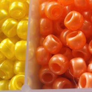 Puede incluir: Primer plano de cuatro contenedores llenos de cuentas de pl&aacute;stico de colores. Las cuentas son en tonos de verde, amarillo, naranja y rosa.