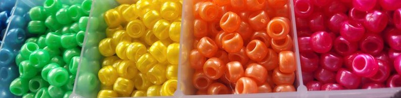 Puede incluir: Primer plano de cuatro contenedores llenos de cuentas de pl&aacute;stico de colores. Las cuentas son en tonos de verde, amarillo, naranja y rosa.