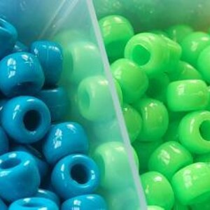 Puede incluir: Primer plano de una variedad de cuentas de pl&aacute;stico de colores en peque&ntilde;os contenedores. Las cuentas est&aacute;n dispuestas en filas de morado, azul, verde, amarillo y naranja.