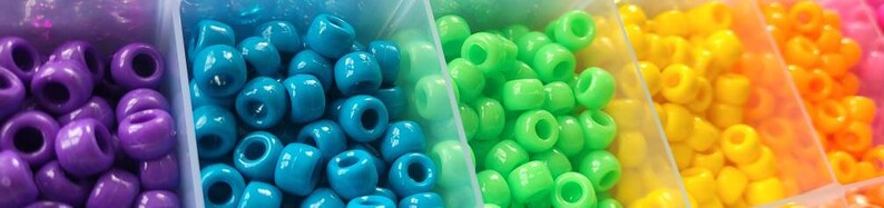 Puede incluir: Primer plano de una variedad de cuentas de pl&aacute;stico de colores en peque&ntilde;os contenedores. Las cuentas est&aacute;n dispuestas en filas de morado, azul, verde, amarillo y naranja.