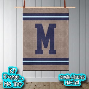 May include: A rectangular crochet wall hanging featuring a large dark blue letter M centered on a tan background. The design includes horizontal stripes in dark blue and light blue at the top and bottom. The piece is suspended from a wooden rod.